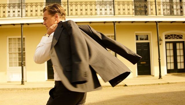 Executive draping suit jacket while walking past historic yellow facade at golden hour