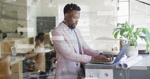Designer Typing at Standing Desk in Bright Modern Office with Laptop and Plans