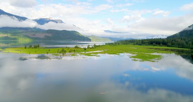 A serene landscape showcases a vast lake reflecting the surrounding mountains and clouds, with copy space. The tranquil setting conveys a sense of peace and the beauty of untouched nature.