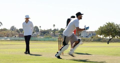Fast bowler charging to deliver ball with umpire watching in sunny cricket match