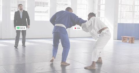 Grappling Judo Partners Sparring on Mats with Referee Observing in Bright Dojo