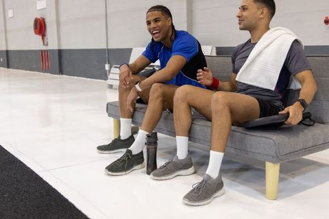 Male teammates laughing and resting on gym bench after training session, casual conversation