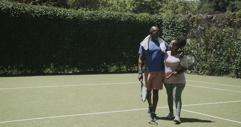 Senior Couple Embracing on Tennis Court with Rackets
