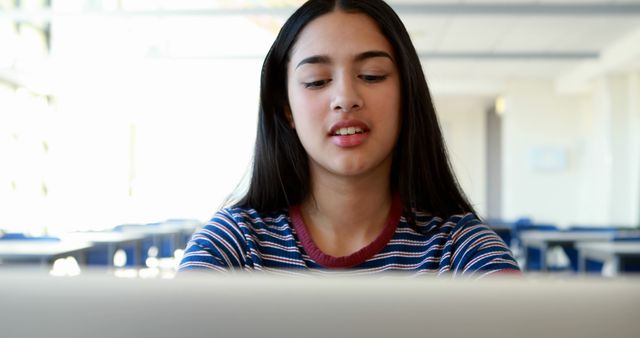 A young Hispanic girl is focused on her work at a computer in a classroom setting, with copy space. Her concentration reflects the importance of technology in education today.