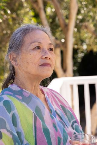 Senior asian woman sitting on sunlit porch gazing upward with serene expression