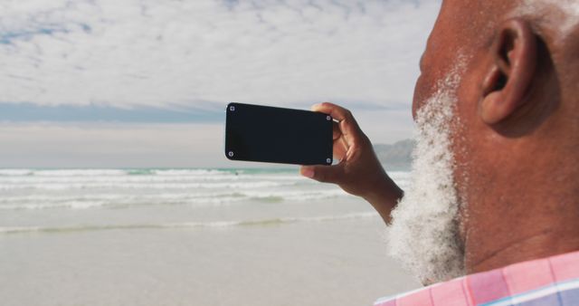Biracial senior man taking a selfie with a smartphone at the beach. healthy outdoor leisure time by the sea.