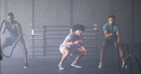 Men engaging in intense battle rope workout at urban gym