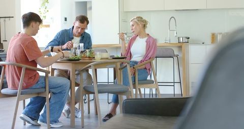 Family sharing healthy salad at modern open-plan kitchen table during casual mealtime together