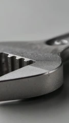 Vertical macro video showing serrated pliers jaw gliding on grey desk revealing metal texture