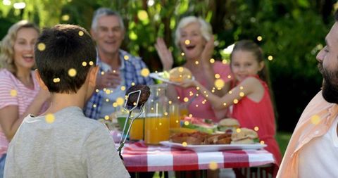 Boy presenting grilled burger at lively multigenerational backyard picnic with bokeh lights