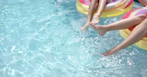 Feet splashing water as women relax on pool floats in sunny pool