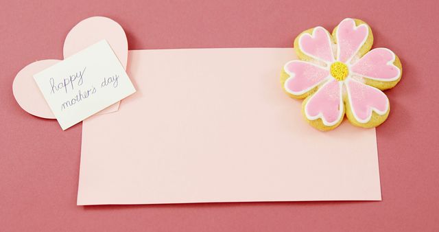 Shows a Mother's Day greeting card on a pink background with a heart-shaped and flower-designed cookie. Ideal for Mother's Day promotions, celebratory messages, and social media posts.