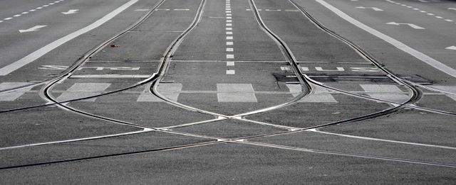 Intersecting tram tracks on an asphalt urban street with road markings. This image showcases city infrastructure, ideal for illustrating urban transportation, public transit systems, and modern city layouts. Great for use in articles about urban planning, public transportation, city driving guides, and infrastructure development.