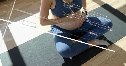 Pregnant woman cradling belly on yoga mat wearing tracker with digital health overlay