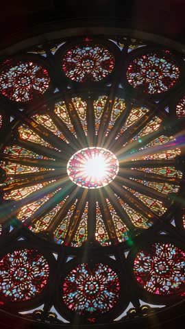 Vertical video capturing sunburst through Gothic rose window casting prismatic rays and lens flares