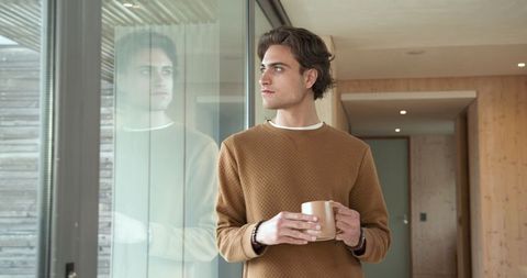 Man holding mug by window in warm toned minimalist hallway