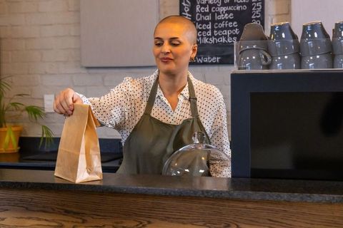Barista placing takeout bag on counter wearing green apron polka dot blouse