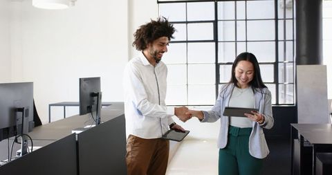 Diverse Coworkers Shaking Hands and Using Tablets in Modern Office