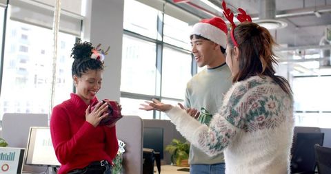 Diverse colleagues celebrating holiday gift exchange in modern open-plan office