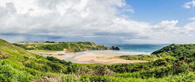 Panoramic view of a lush coastal landscape with green hills, sandy beach, and dramatic cliffs jutting into the ocean. Perfect for travel brochures, outdoor adventure advertisements, vacation planning materials, and nature conservation campaigns.
