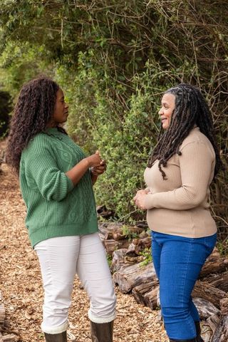 Two african american women conversing on woodchip trail in forest wearing cozy sweaters