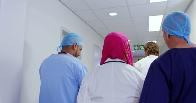 Medical professionals are walking together in a hospital corridor. One wears a pink hijab, indicating diversity among the team. This could be used to depict themes of teamwork, diversity in healthcare, and hospital environment. Ideal for medical institutions, healthcare advertisements, and articles related to medical staff.