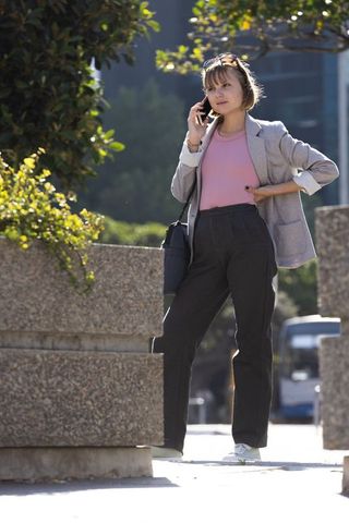 Young professional talking on smartphone in city plaza wearing blazer and shoulder bag