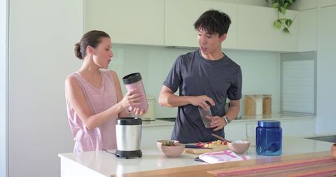 Multicultural couple preparing smoothies and fruit snacks at bright modern kitchen island