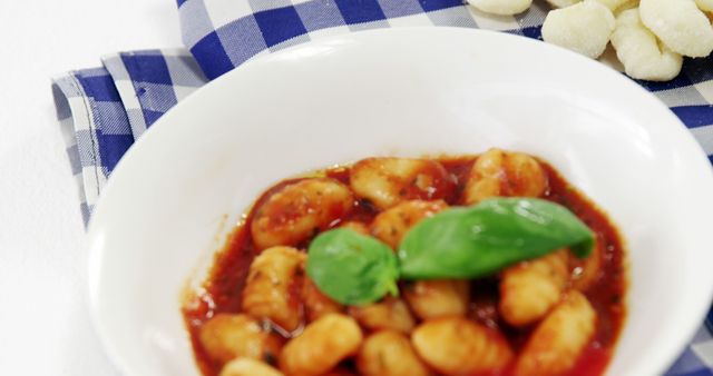 A traditional Italian gnocchi dish is served with tomato sauce and basil on a checkered cloth. - Download Free Stock Photos Pikwizard.com