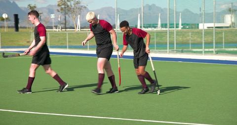 Young male field hockey players walking on turf in team uniforms