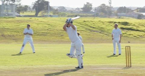 Cricketer hitting powerful swing with fielders standing by