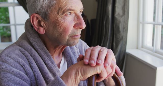 Senior Man Pondering Deeply by Window Holding a Wooden Cane - Download Free Stock Images Pikwizard.com