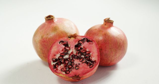 Closeup of fresh pomegranates with one cut in half, showcasing the juicy seeds inside. Ideal for use in food photography, health-related content, recipes, grocery marketing, and nutrition blogs. Perfect for promoting healthy eating and natural antioxidants.