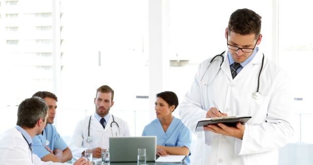 Group of medical professionals in formal discussion with a doctor taking notes on a clipboard. Ideal for promoting teamwork, hospital services, healthcare consultations, collaborative environment, and medical office settings.