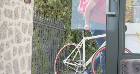 Male pushing white bicycle with red rims through stone doorway at residential entrance
