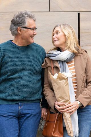 Senior couple smiling holding bouquet by urban stone wall casual fall fashion