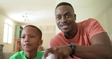 African american father and son playing video games on sofa sharing laughs and bonding
