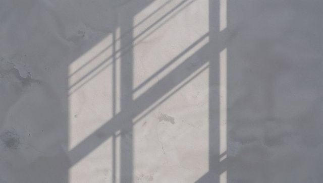 Window shadow grid casting on weathered plaster wall in soft daylight