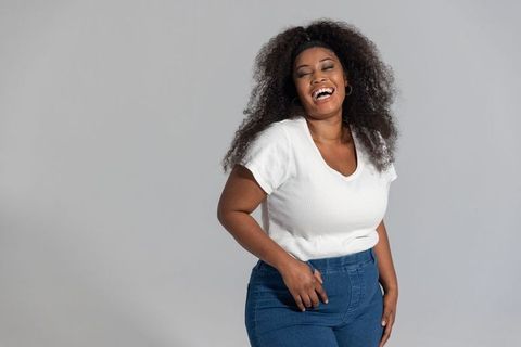 Confident african american woman laughing and posing in studio wearing white top and jeans
