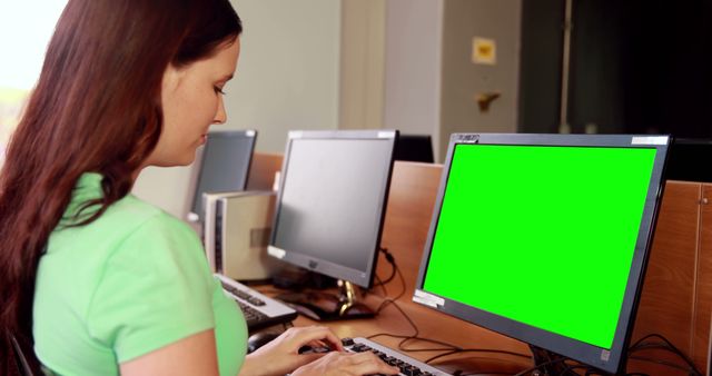 A young Caucasian woman is working on a computer with a green screen monitor, with copy space. She appears focused on her task, which could involve programming, graphic design, or data entry.