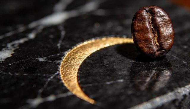 Resting roasted coffee bean on black marble with gold crescent macro still life