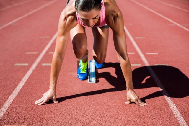 Female athlete in starting position on running track, preparing for a sprint. Ideal for use in sports-related content, fitness motivation, athletic training programs, and advertisements promoting physical fitness and competitive sports.