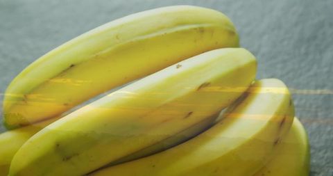 Bunch of ripe yellow bananas resting on textured gray counter reflecting warm light