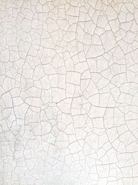 Close-up view of a wall with cracked white paint producing a textured, distressed appearance. Ideal for use in backgrounds, design projects needing a vintage or rusty effect, and advertisements featuring rugged or aged themes.