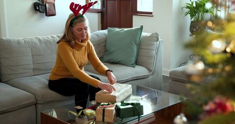 Woman with antler headband wrapping gifts in cozy living room
