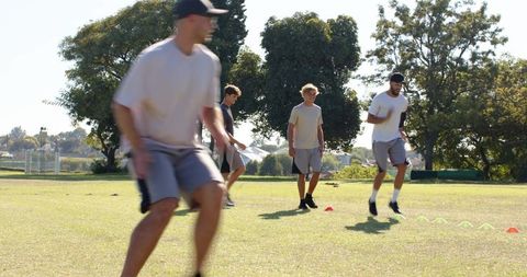 Male athletes practicing agility cone drills and jogging in sunny suburban park session