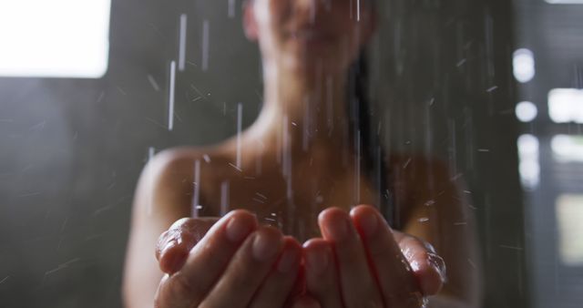 Image of a woman standing in a shower, hands outstretched catching water. Ideal for use in campaigns and materials related to self care, wellness, hygiene, and relaxation. Can also be used on blogs and magazines that focus on daily routines, mental health, and spa services.