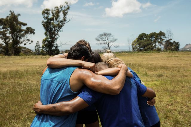 This image shows a group of fit individuals embracing each other in an outdoor bootcamp setting. Ideal for use in fitness blogs, team-building articles, motivational posters, and health and wellness promotions.