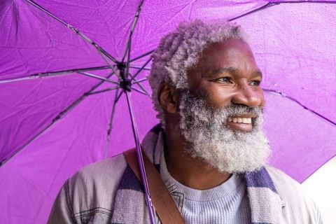 Joyful senior bearded man holding purple umbrella in gentle rain, smiling outdoors