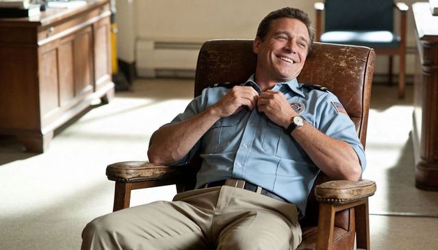 Smiling police officer buttoning uniform while relaxing in sunlit station office